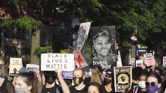 A crowd marches down Monument Avenue raising protest signs proclaiming “Black Lives Matter,” and “No Justice, No Peace.” Another sign features a large portrait of Breonna Taylor, a 26-year-old Black woman shot and killed by police in Louisville on March 13, 2020.